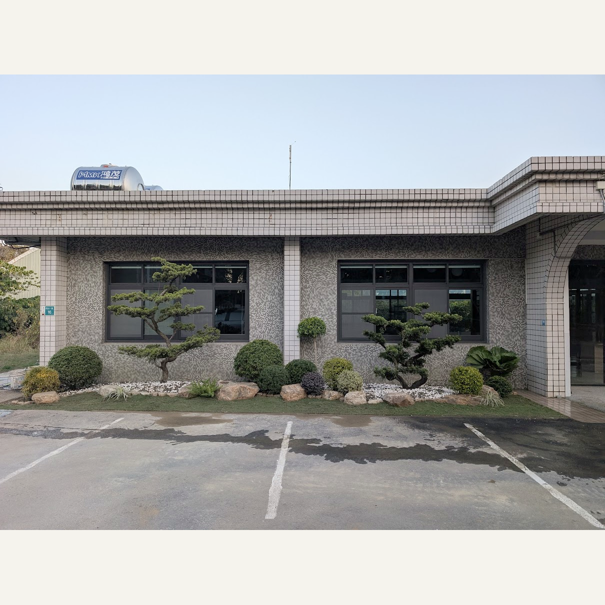 建築正面窗前配置造型樹、圓整灌木、白色石粒與景石