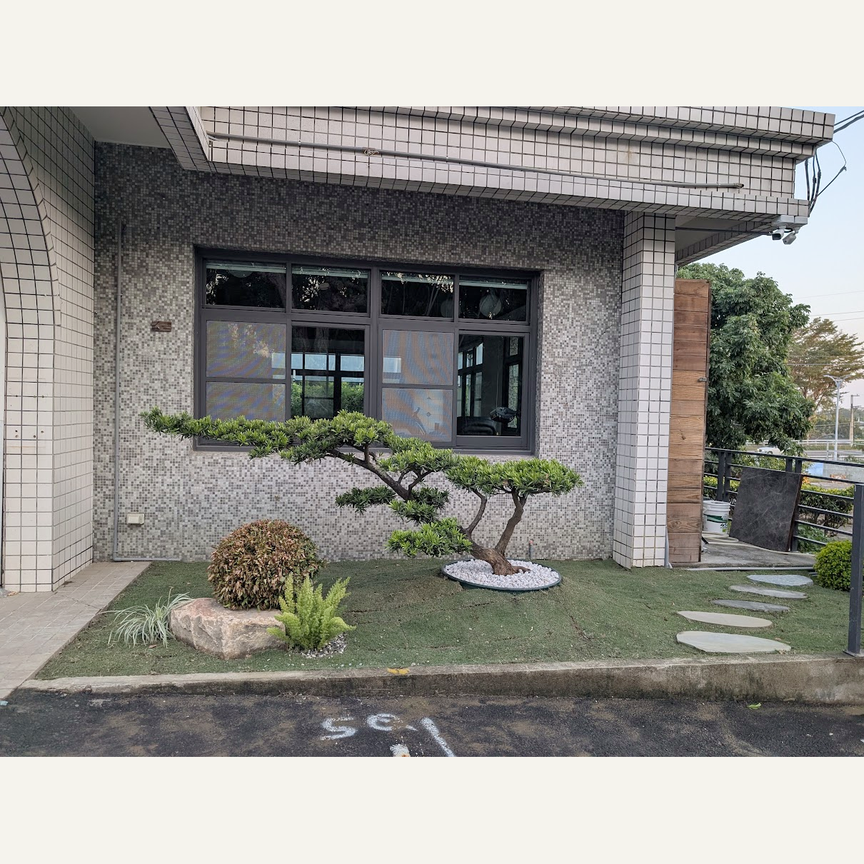 入口旁橫向伸展的造型樹,搭配白石、景石與低矮植栽
